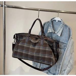 Détail du sac de voyage à carreaux avec poignées en cuir marron et bandoulière réglable