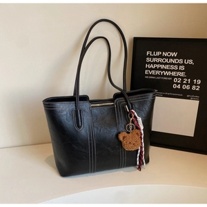 Detailed close-up of a black tote bag featuring white stitching and bear charm