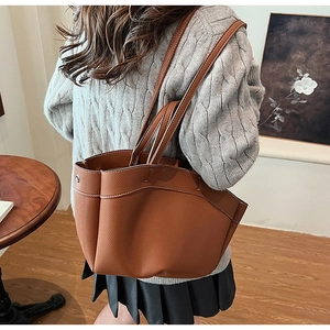 Brown leather tote bag with white contrast stitching worn by a model in a cozy setting