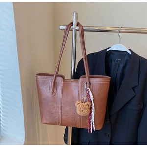 Detailed view of brown tote bag with contrast stitching and teddy bear charm