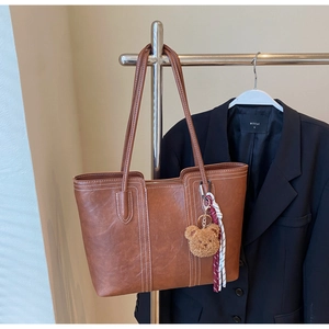 Detailed close-up of brown PU tote bag featuring white contrast stitching and bear charm