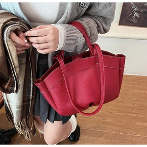 Detail of red pebbled leather tote bag with fine stitching and slim handles