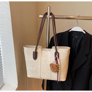 Beige tote bag detail showing brown contrast handles with bear charm and silk scarf