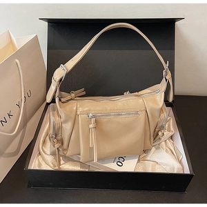 Détail d'un sac à bandoulière beige brillant avec zips dans un coffret cadeau de luxe
