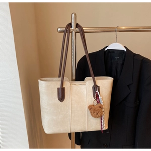 Detail of off-white tote bag with brown straps, bear charm, and plaid scarf accessory