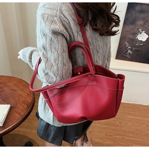 Detail of red pebbled leather tote bag with white contrast stitching on round handles