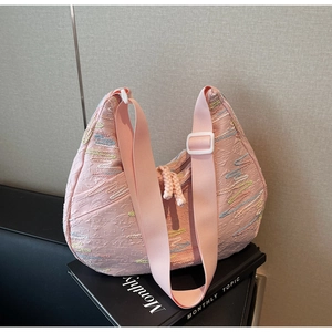 Close-up of pink crescent tote bag featuring colorful textured stripes and wide woven strap