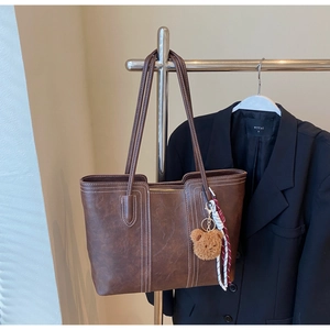 Detail of dark brown leather tote bag with white stitching and plush bear charm
