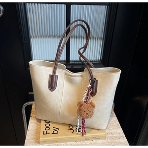 Detail of cream tote bag with brown straps and cute bear charm on a book