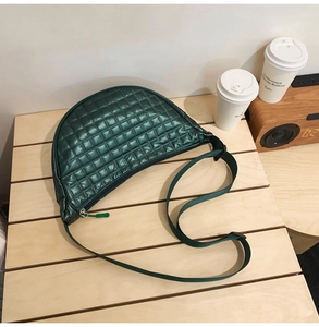 Nahaufnahme einer dunkelgrünen gesteppten Halbmond-Tasche aus Nylon auf Holztisch