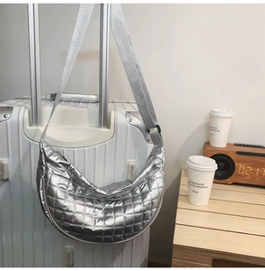 Detailaufnahme einer silbernen Stepptasche in Halbmondform an einem Koffergriff