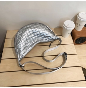 Detailansicht der silbernen gesteppten Halbmondtasche mit Metallic-Finish auf Holz