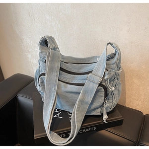 Detail of light blue denim crossbody bag with multiple zippers on a leather sofa