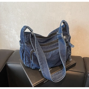 Detail of dark blue denim shoulder bag with multi-zipper layers and wide strap
