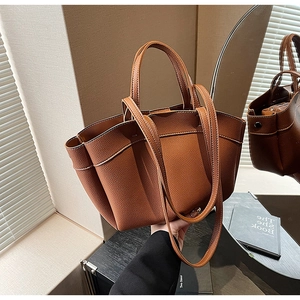 Detail of caramel pebbled leather tote bag showing side pleated structure and dual handles