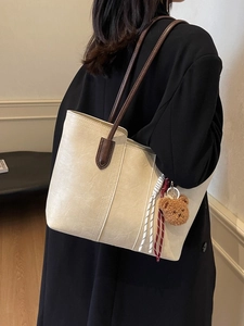 Cream tote bag with brown straps and teddy bear charm shown on model's shoulder