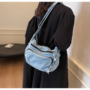 Detail of light blue denim crossbody bag with multiple zip pockets and wide strap
