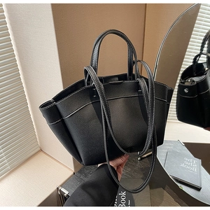 Detail of black lychee grain leather tote bag with white contrast stitching and long strap