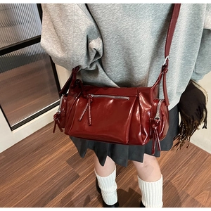 Détail d'un sac bandoulière en cuir verni bordeaux avec zips et longs pompons