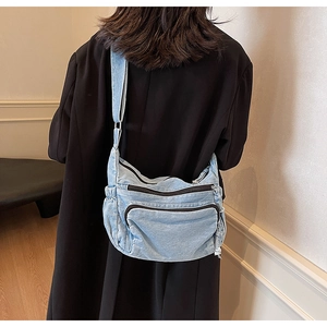 Back view of light blue denim messenger bag with multi-zipper pockets on a black coat