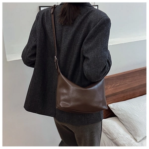 Detail of dark brown leather tote bag with adjustable strap worn with a grey blazer
