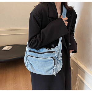 Detail view of a blue denim crossbody bag with multiple zip pockets and a wide shoulder strap
