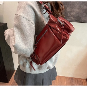 Sac bandoulière en cuir verni rouge foncé porté par un mannequin au look moderne