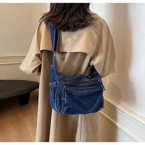 Detailed view of dark blue denim crossbody bag with multiple zippers shown on a model