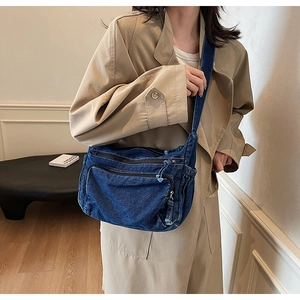 Detailed side view of washed blue denim crossbody bag featuring pleated design and wide strap