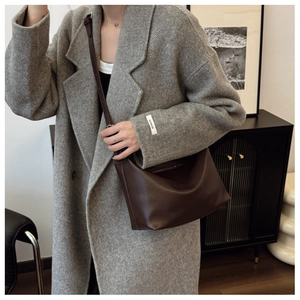 Brown leather half-moon tote bag styled with a grey coat in a minimalist interior