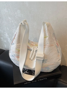 White pleated hobo bag with colorful embroidery and wide strap on minimalist display