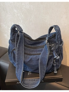 Vintage dark blue denim shoulder bag with multi-pocket design and wide strap on black sofa