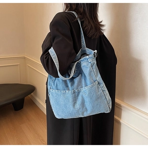 Detail showing the light blue denim tote bag with two practical front pockets on model