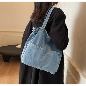 Detail of light blue denim tote bag with external pocket and metal ring on the strap