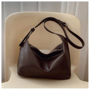 Detail of dark brown leather hobo bag with adjustable strap on a minimalist chair