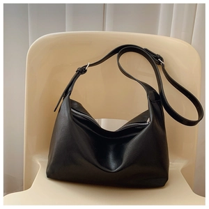 Detail of a black leather dumpling bag with silver zipper on a minimalist chair