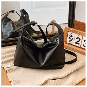 Detailed close-up of glossy black leather tote with silver zipper and adjustable strap