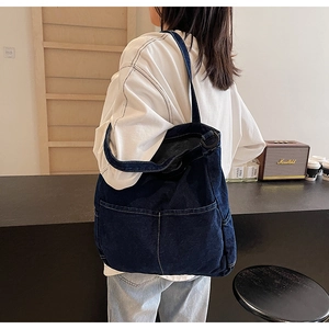 Detail of a large blue denim tote bag with visible stitching worn by a model in a cafe