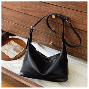 Detail view of large black crescent tote bag with adjustable strap on a wooden drawer