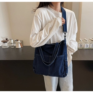 Detail view of large blue denim crossbody tote bag with adjustable strap and front pockets