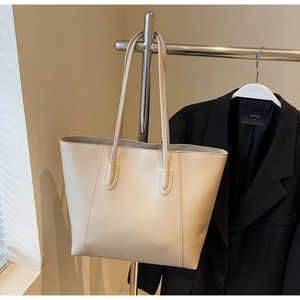 Detailed close-up of a beige PU leather tote bag hanging against a dark blazer backdrop