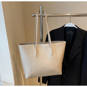 Detail of minimalist cream tote bag with fine stitching on sleek leather surface