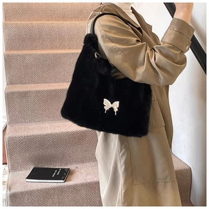 Detail of a plush black faux fur shoulder bag with white butterfly buckle on a model