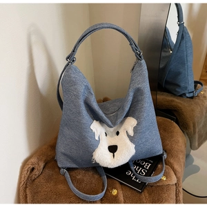Detail of blue denim hobo bag featuring a cute white plush puppy patch and metal buckle