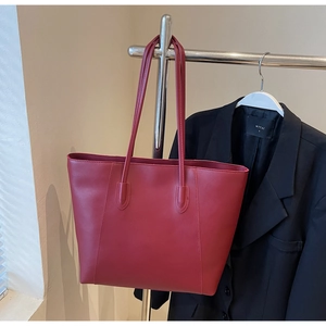 Detail of burgundy leather tote bag hanging on a hanger next to a black blazer coat