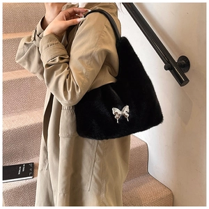 Detail of black plush shoulder bag featuring a silver liquid metal bow and leather strap