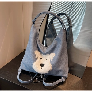 Detailed close-up of blue denim tote bag with white fluffy dog embroidery on wood surface