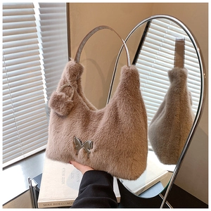 Detail of plush brown tote bag featuring a silver butterfly buckle and furry ball charm
