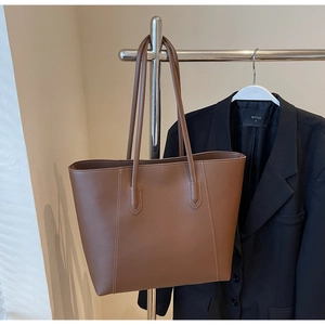 Detail of brown leather tote bag with elegant white contrast stitching and slim straps