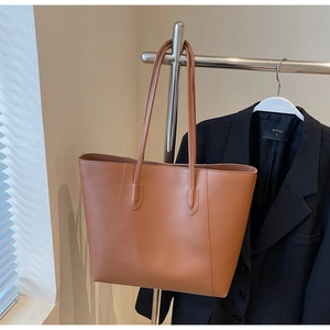 Brown faux leather tote bag hanging on a rack with classic office attire background